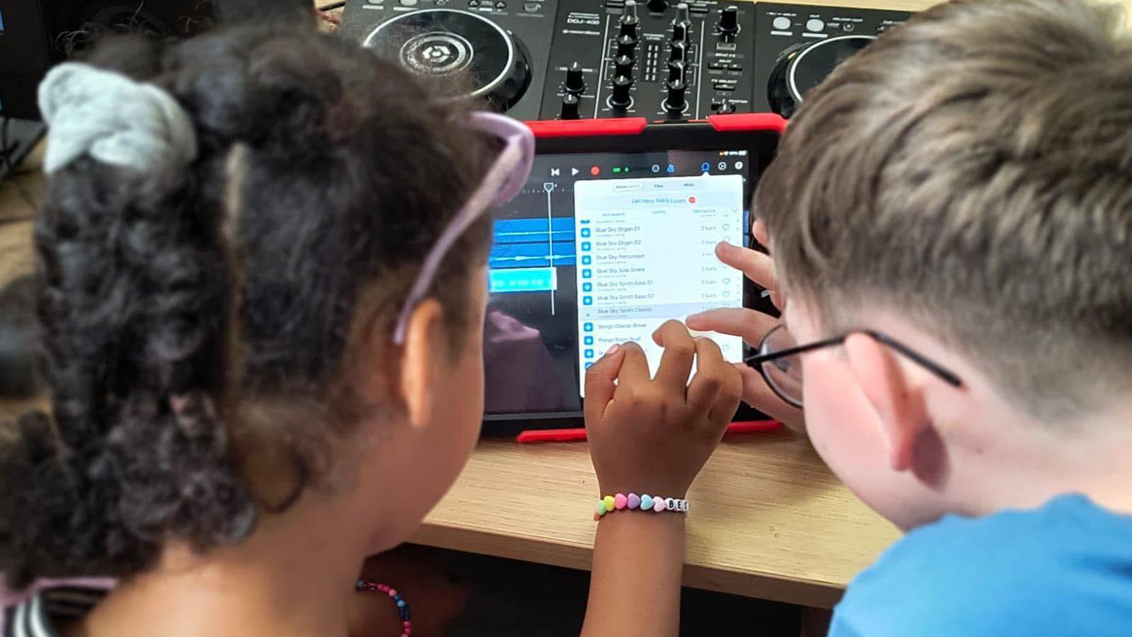 Two children working on a tablet computer, doing some sound editing.