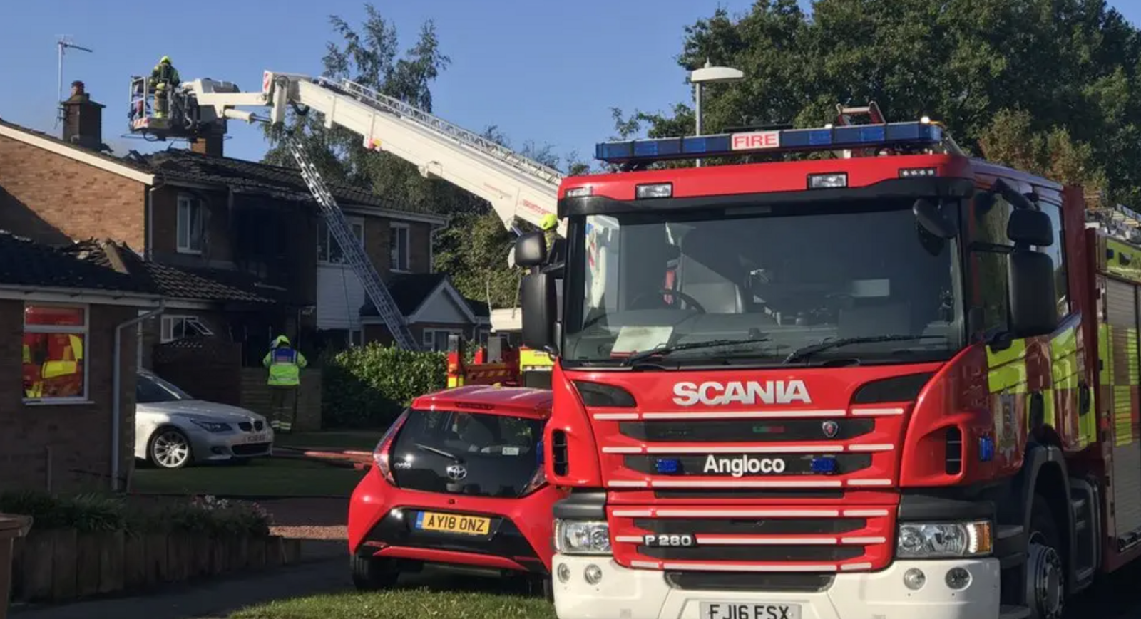 A fire engine parked in a residential road. Firefighters can be seen tending to house.