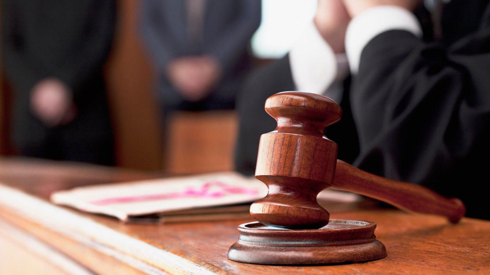 A wooden gavel, on a court desk, by papers, with a hands arms blurred, a stock image