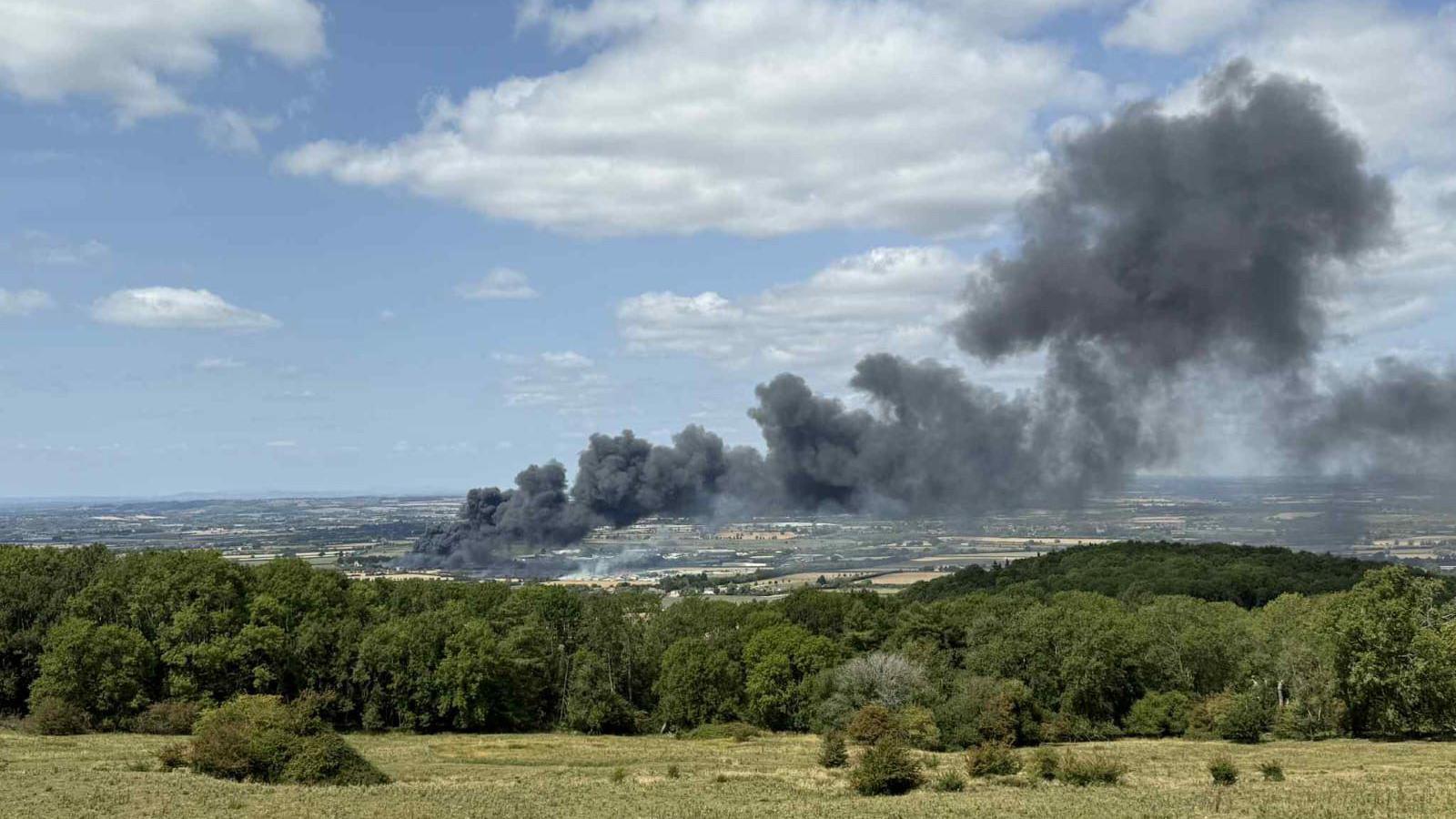 Black smoke billowing into the sky from a number of fields behind a tree line