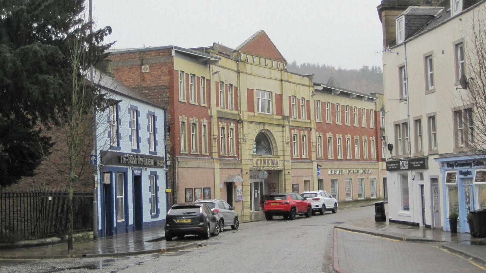 A different angle view of the Pavilion Cinema on a wet day in Galashiels with cars parked in front of it with its yellow and brick facade.
