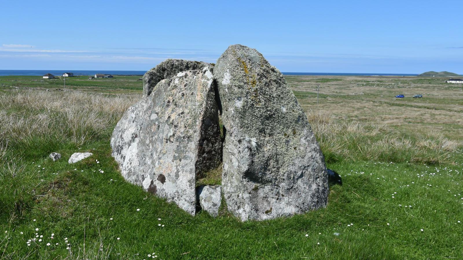 Large rocks have been grouped together. The monument is in a grassy field. the sea is in the distance.