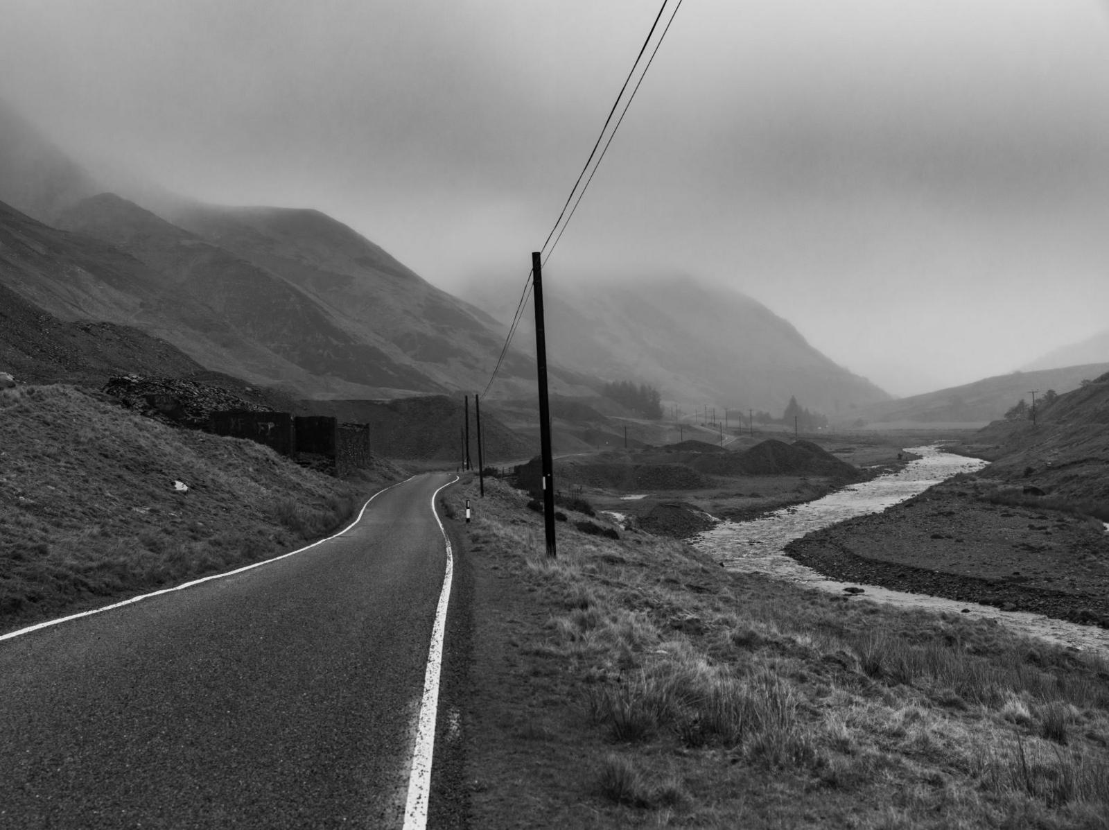 A black and white photograph of a country road surrounded by misty mountains in Cwmystwyth, Ceredigion.