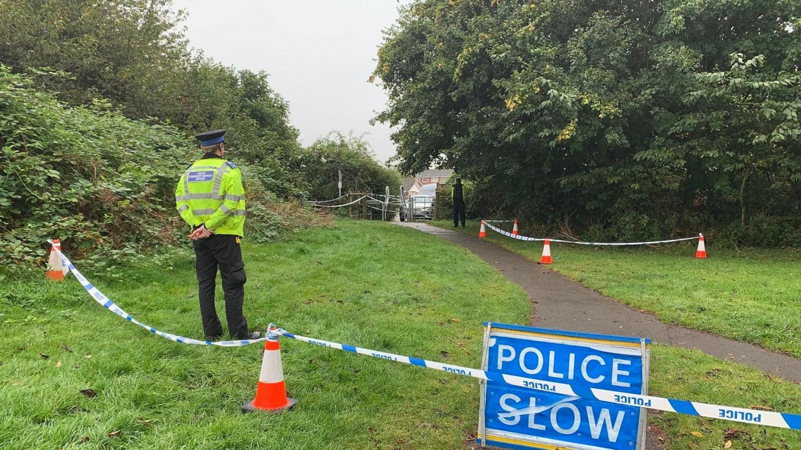 A police officer standing behind a line of police tape in a park