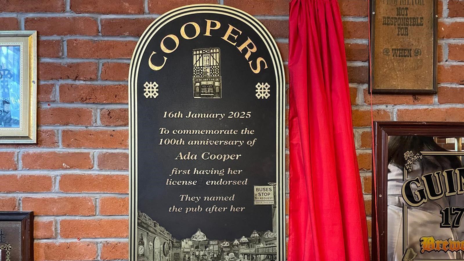 Commemorative plaque on wall reading Coopers, 16th January 2025, To commemorate the 100th anniversary of Ada Cooper first having her license endorsed. They named the pub after her.