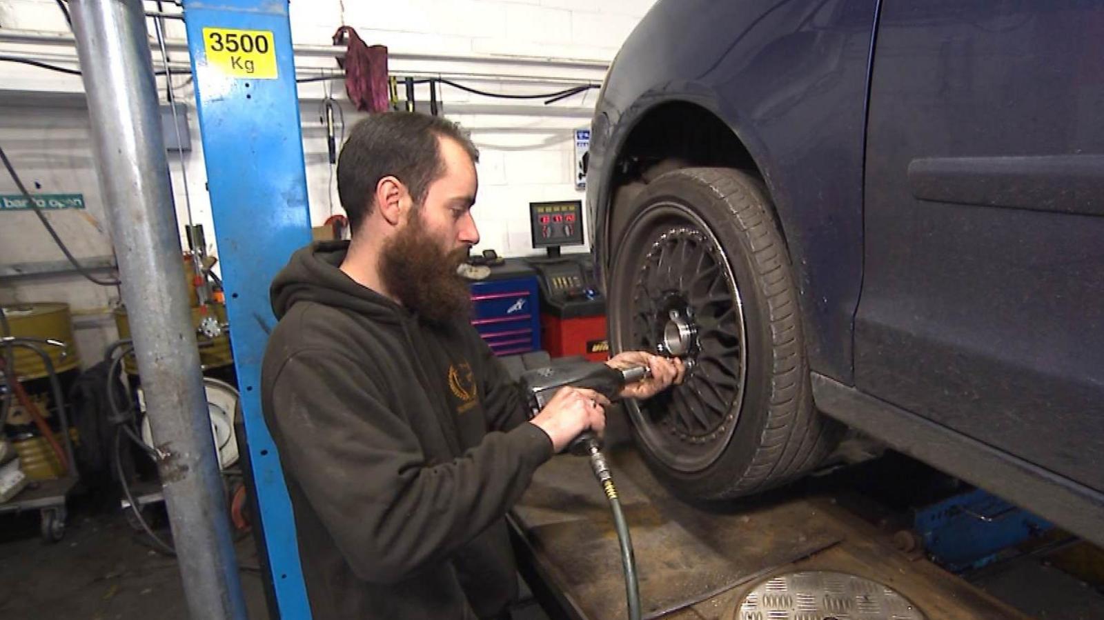 James Forrester, managing director of Paramount Garage in Dartford, in a workshop, using a pneumatic machine on the wheel nuts of a car tyre up on a ramp