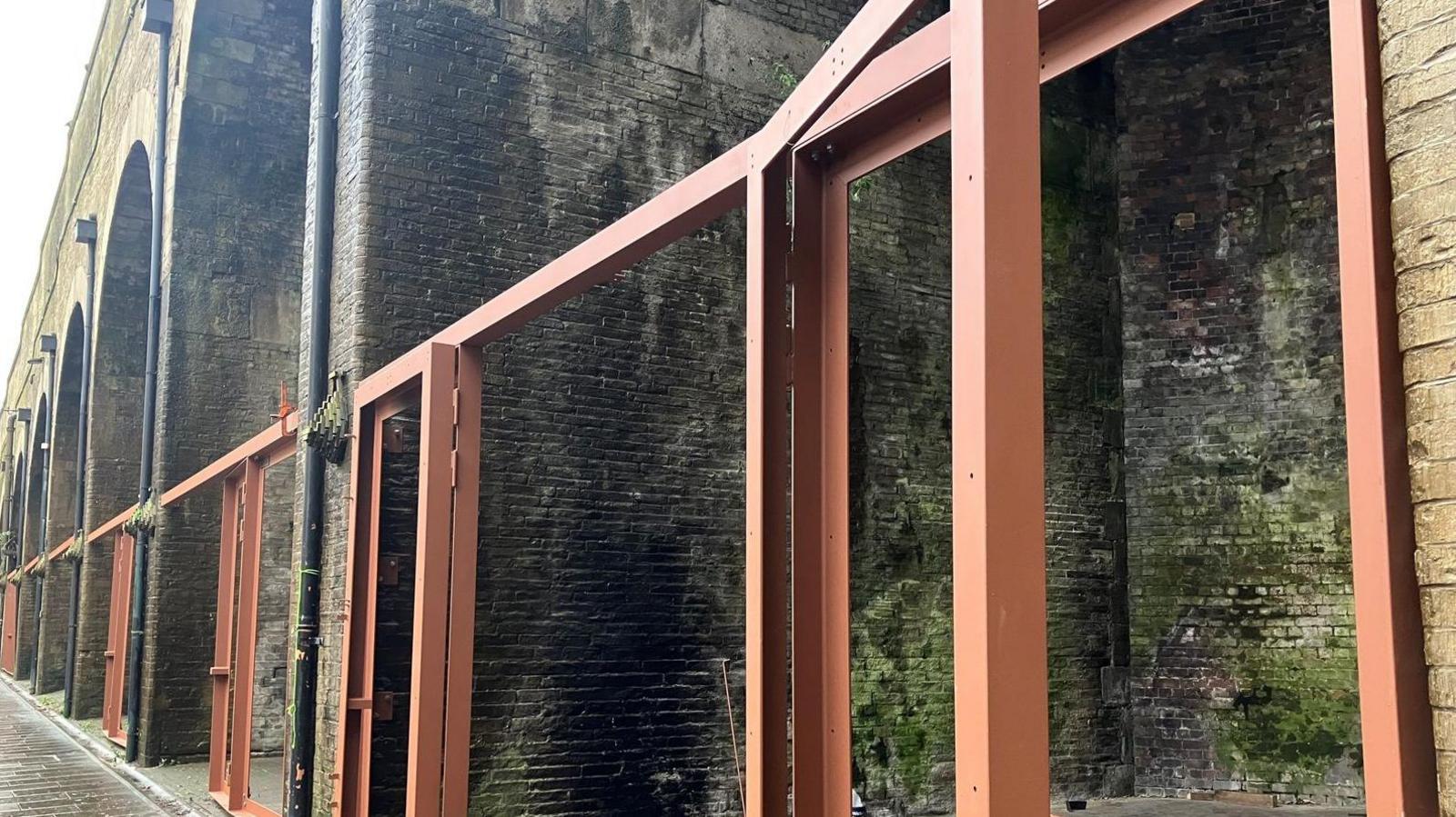 A row of brick railway arches with brown metal frames installed