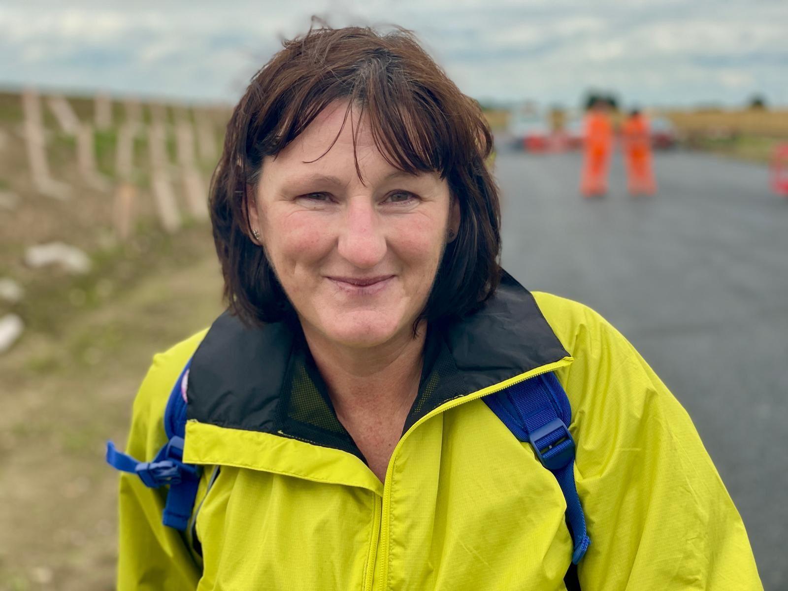 Sarah Wratten in a yellow jacket smiles at the camera as she stands on the new road.