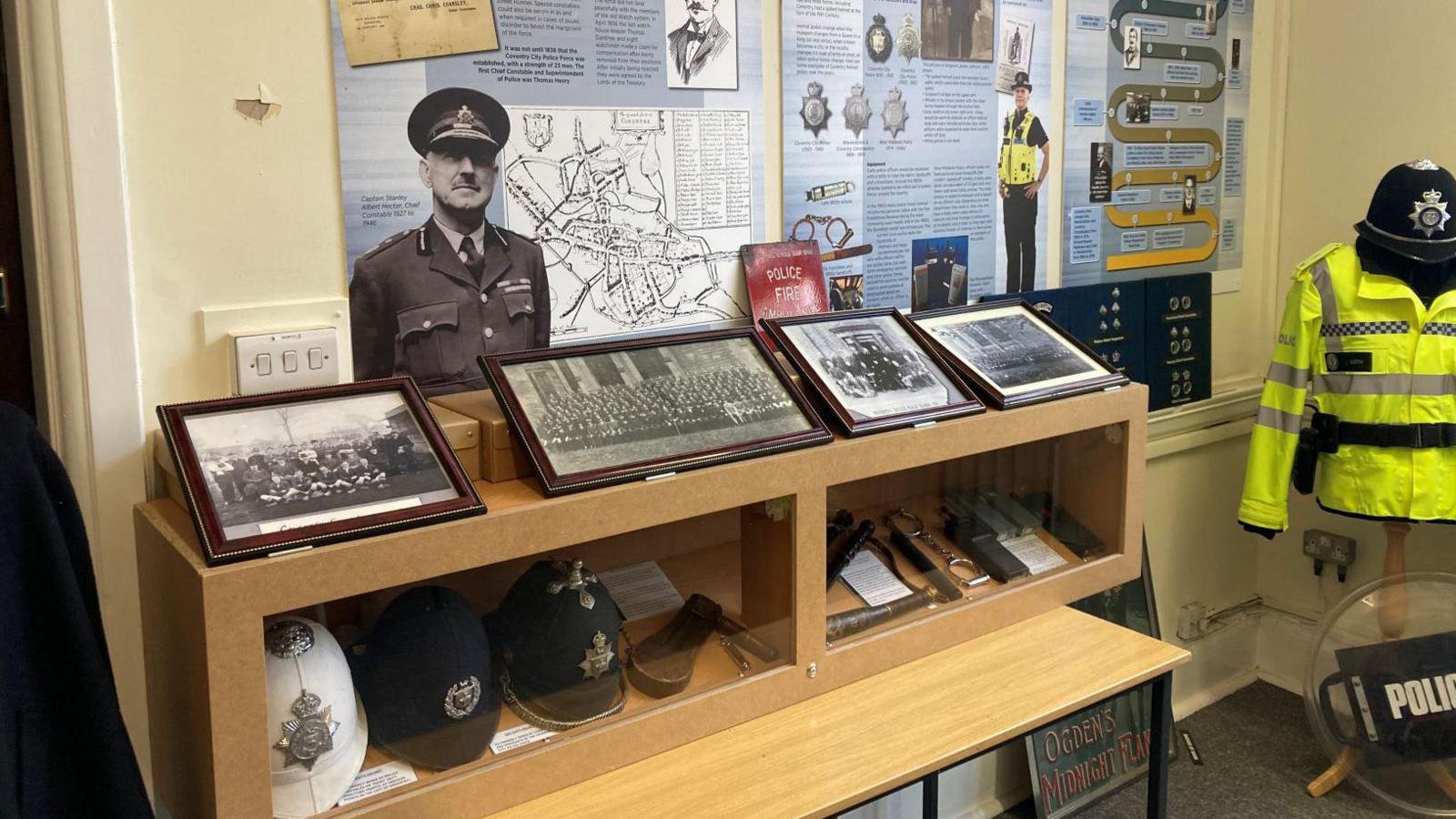 A museum display showing photographs of police officers, handcuffs, truncheons and a yellow high-vis jacket