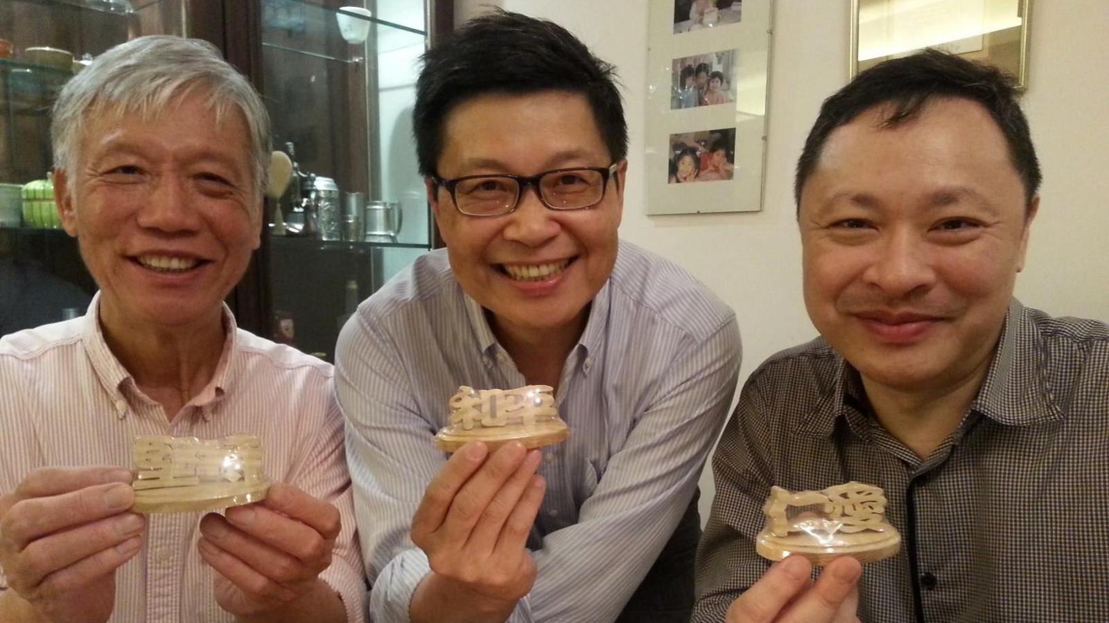 Chu Yiu-ming, Chan Kin-man and Benny Tai in 2013 smiling and holding up a birthday gift of wood carvings spelling out "persevere, peace, love"