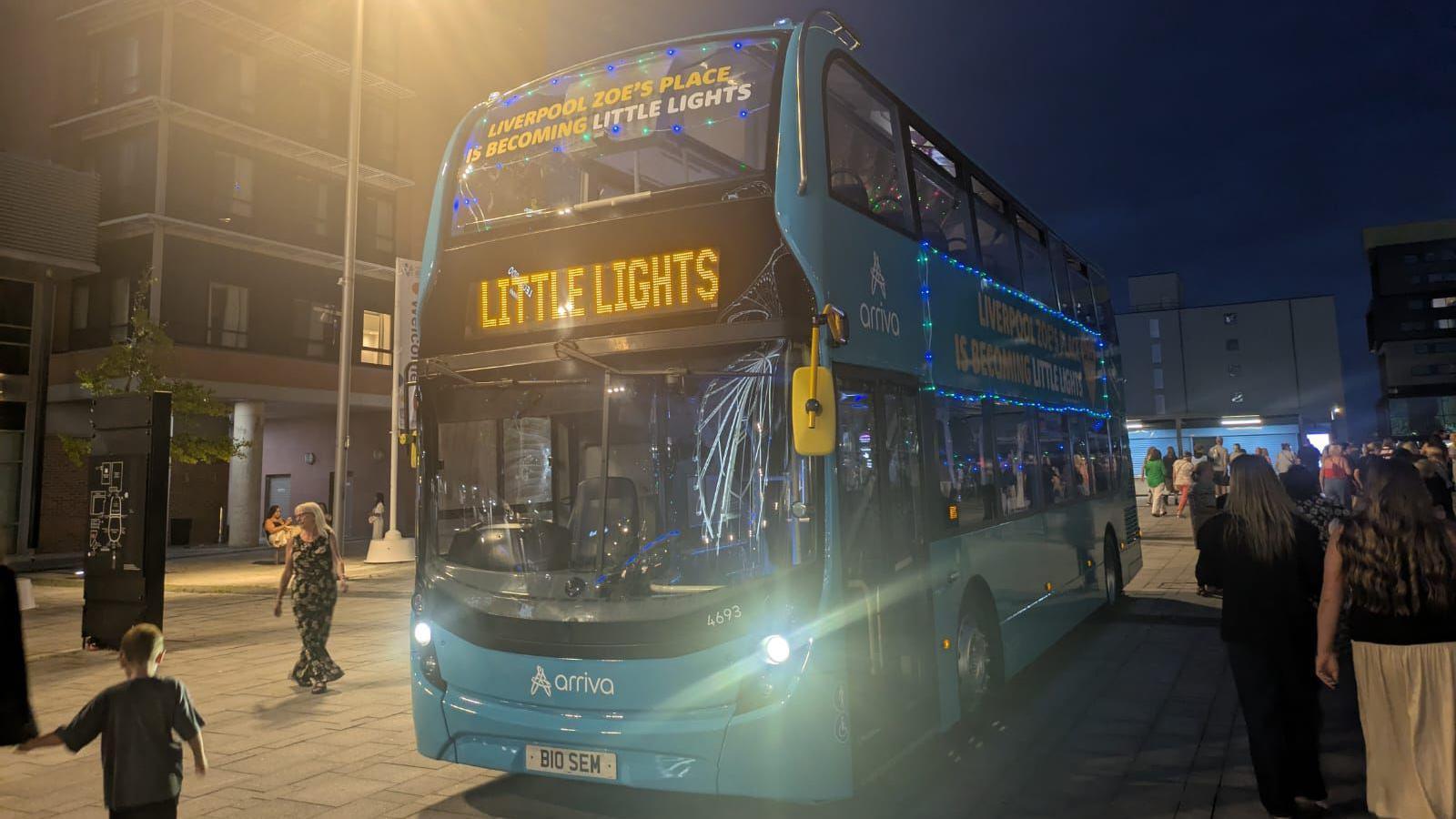 A double decker bus has the words 'Liverpool's Zoe's Place is becoming Little Lights' written on it, with 'Little Lights' on the vehicle's destination screen.
