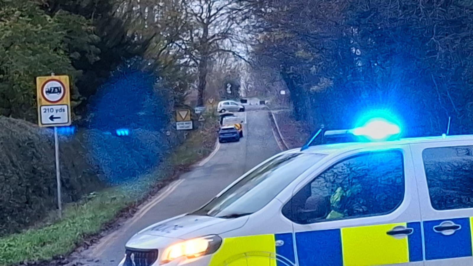 A police van on a country road with a blue car and a few other vehicles in the foreground