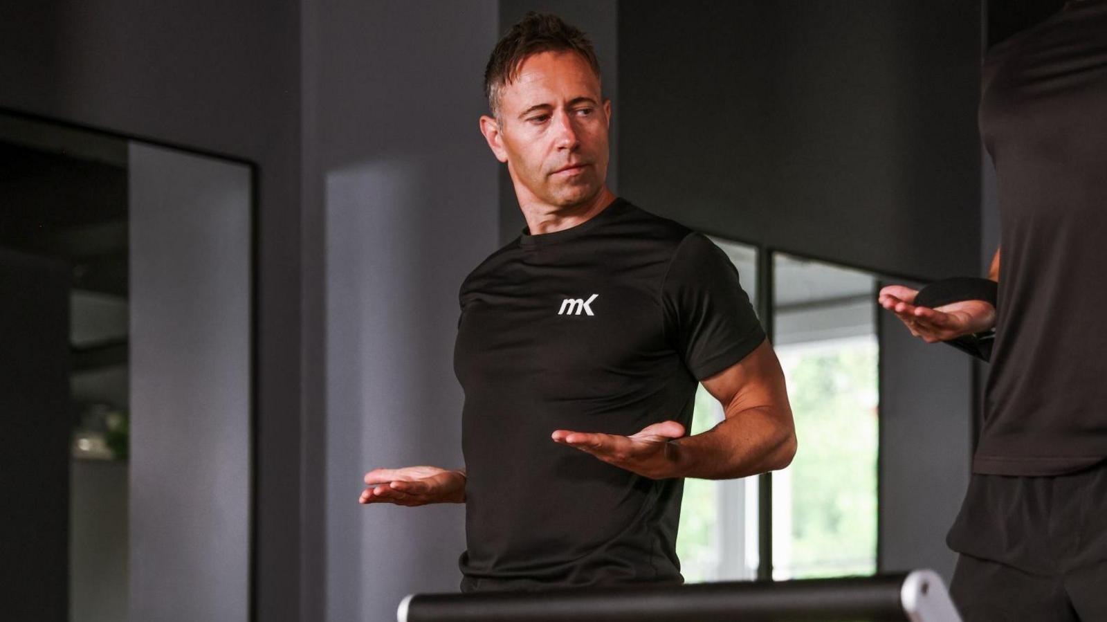 Matt Kendrick trains another man at MK Health Hub. They are both wearing black. They are holding their hands out as they do a fitness exercise.