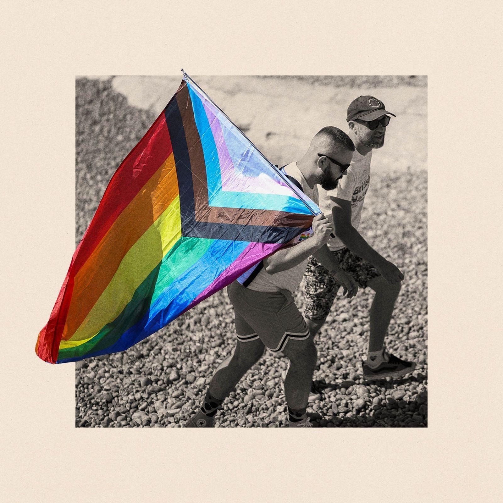A black and white photograph of two people walking outside, one of the men is holding a pride flag, with another man walking next to him in a baseball cap 