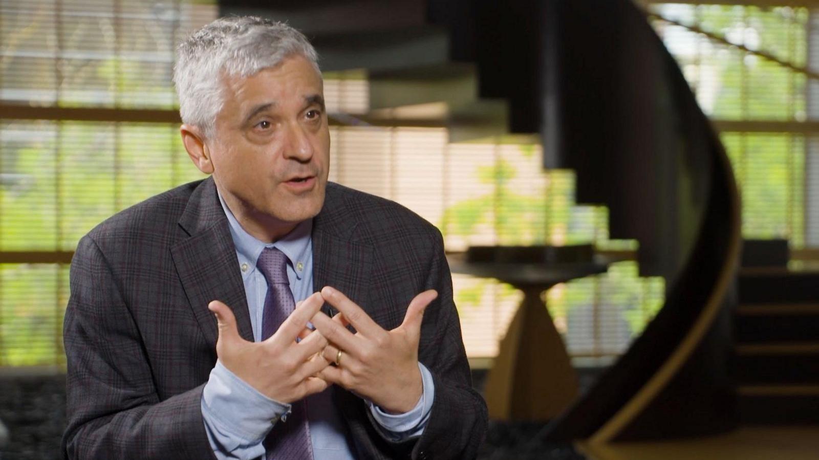 Steven Levitsky wears a grey suit with blue shirt speaking inside a room