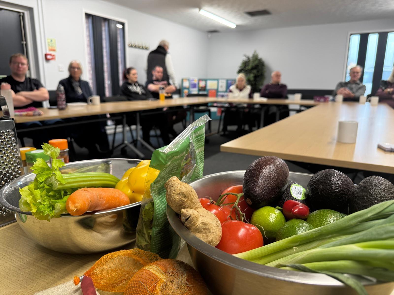 Bowls of fresh vegetables stand in the foreground and students are in the background