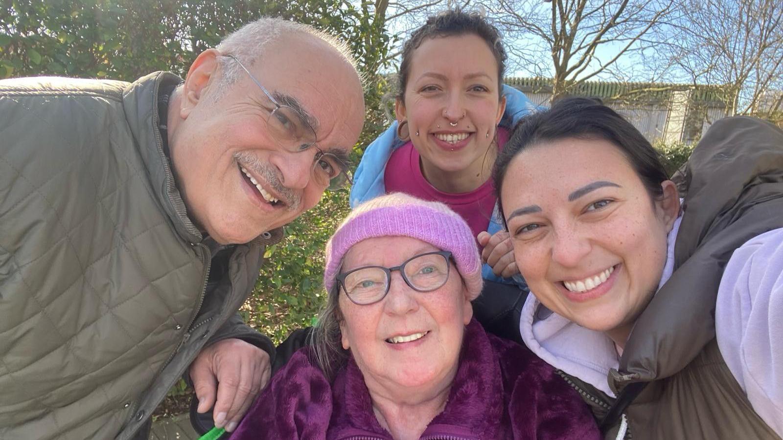 Ms Elnagy, wearing a pink top and blue jacket, with her dad, who is wearing a khaki jacket and light framed glasses, her sister who is wearing a black gilet and her mum who is weating a pink hat and dark-framed glasses with a pink coat. They are all smiling at the camera 