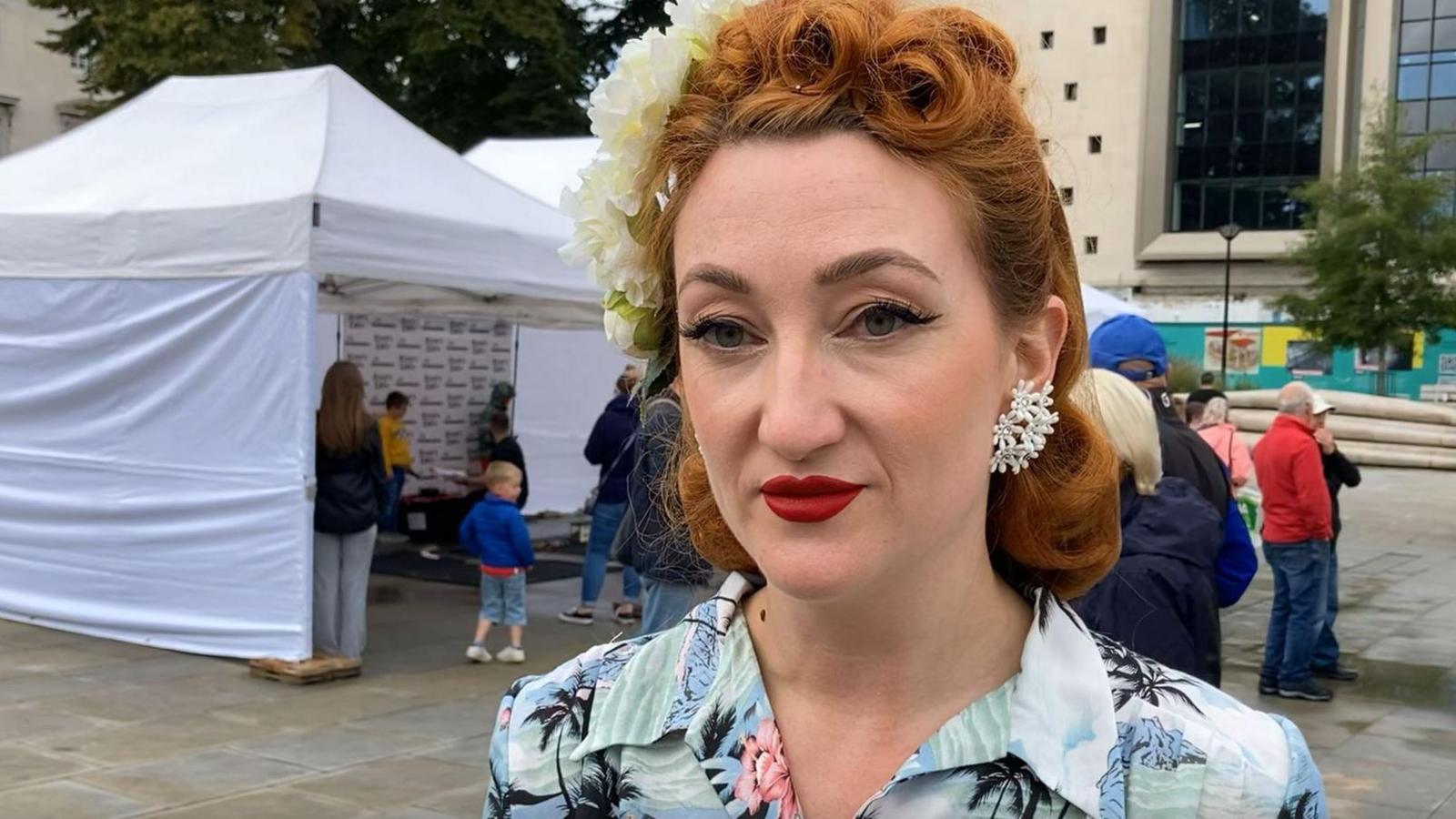 Woman looking into camera with vintage hairstyle in curls, flowers in hair and retro make-up