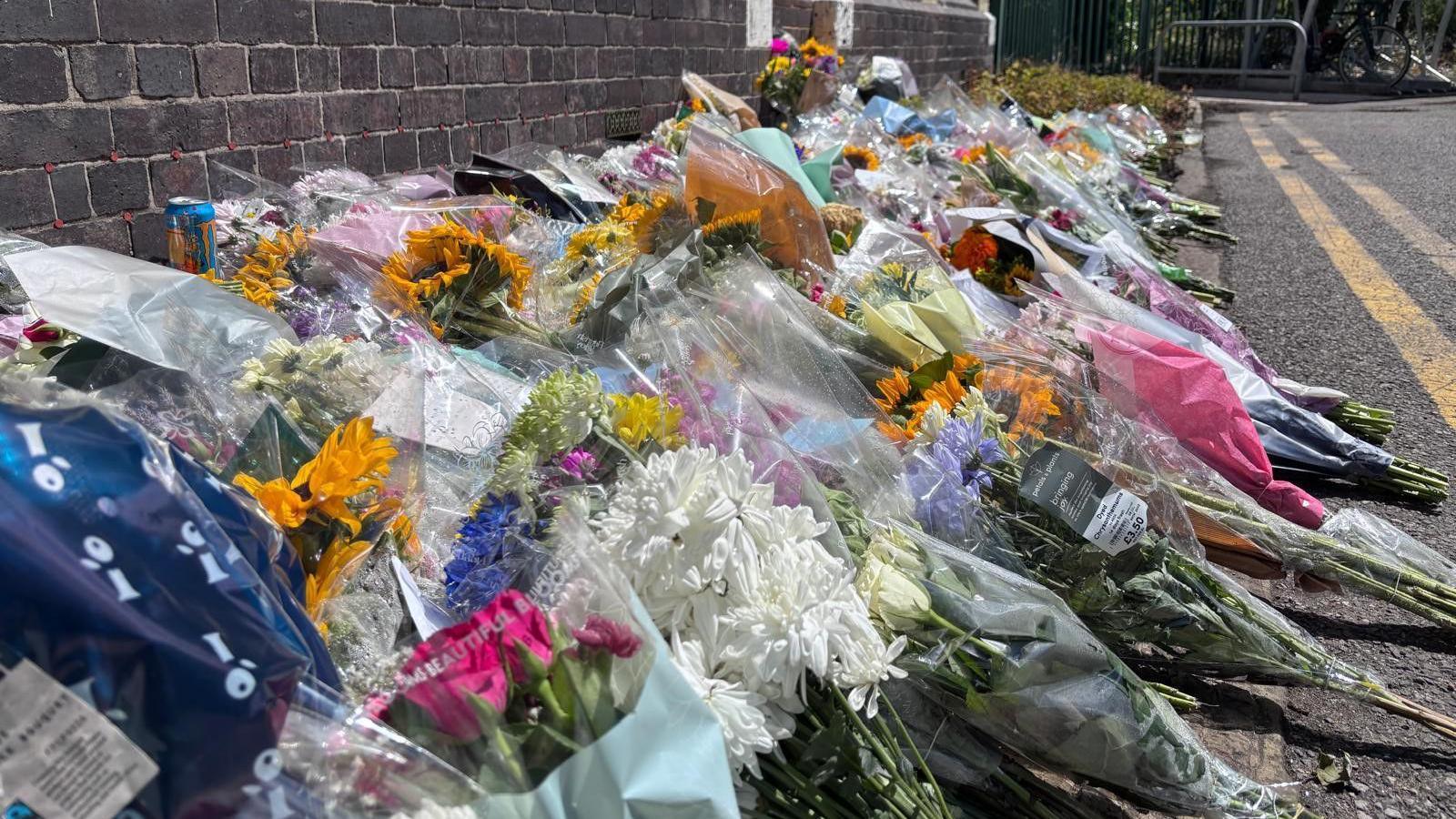 Dozens of bunches of flowers are lined up on the road against a brick wall.