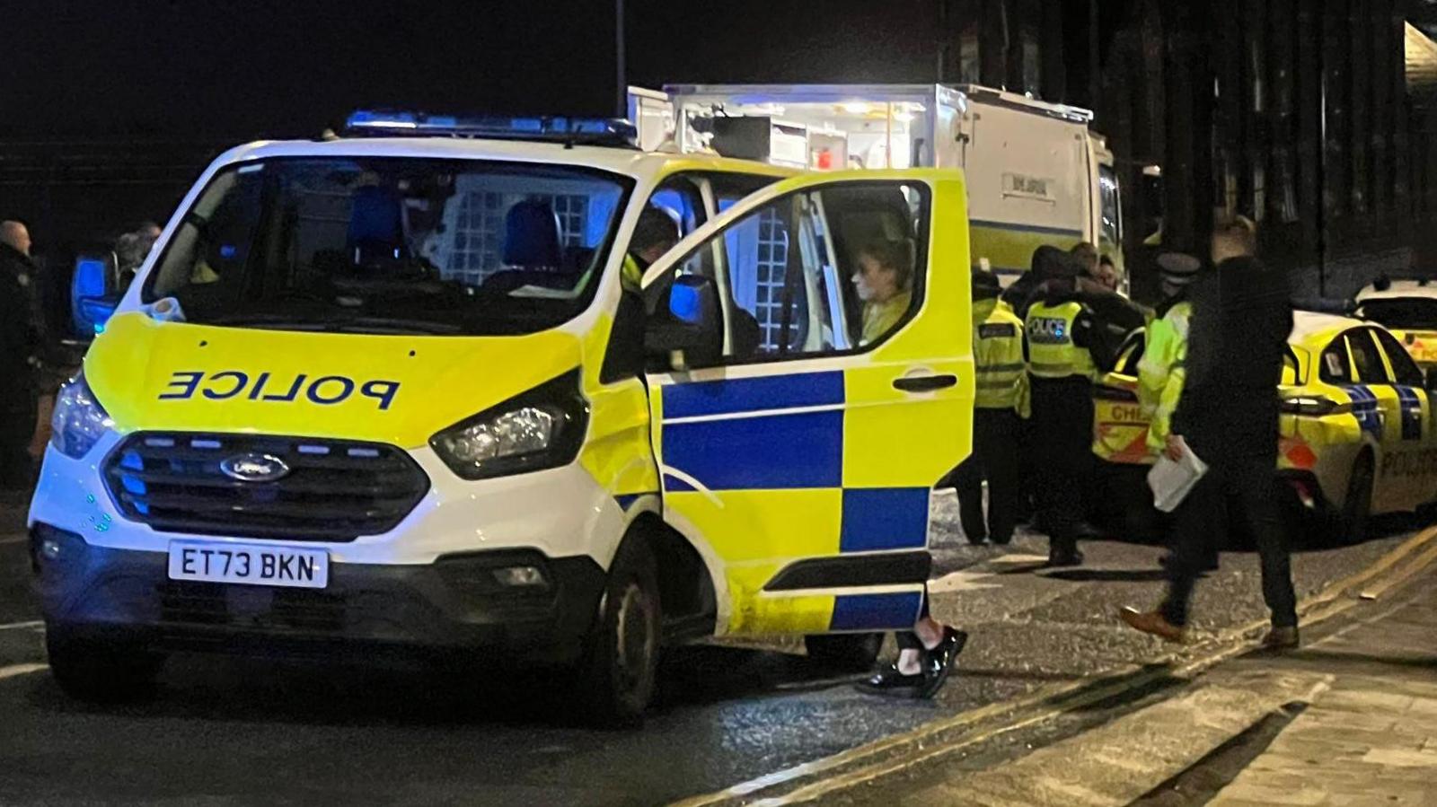 A liveried police van is parked near Chester railway station, along with other police cars. Several officers can be seen standing in the road.