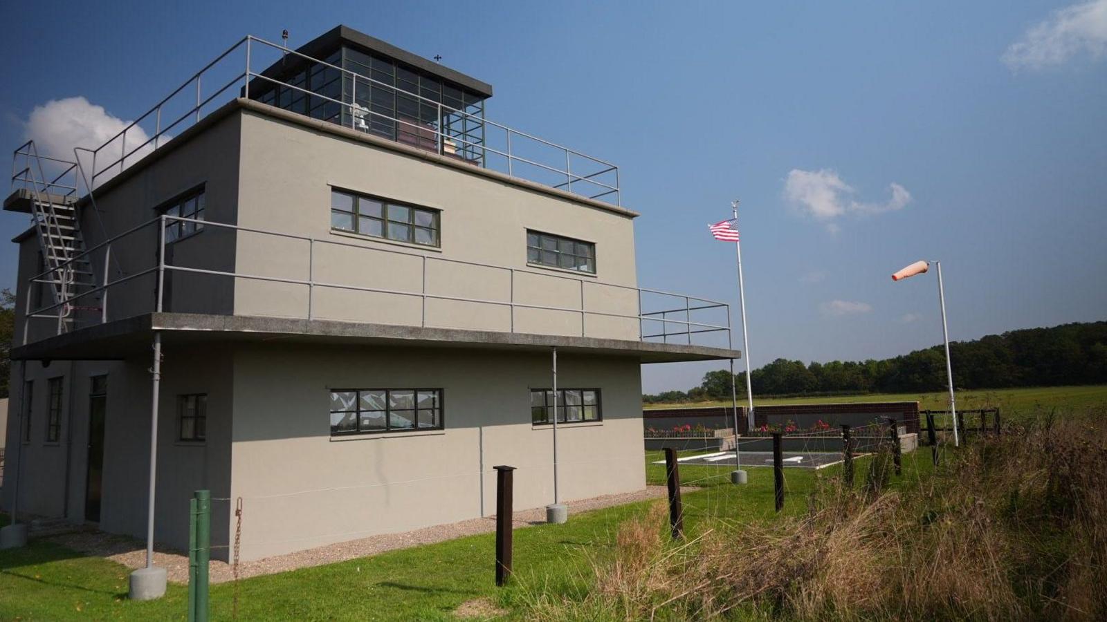 A large three-storey grey control tower with balconies in a field.