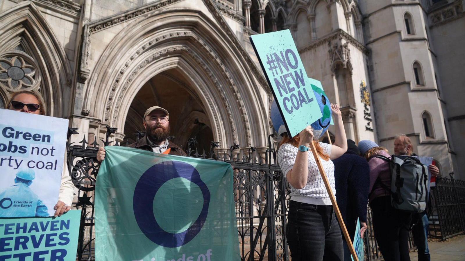 People holding signs and banners, saying "no new coal" outside a grand building.