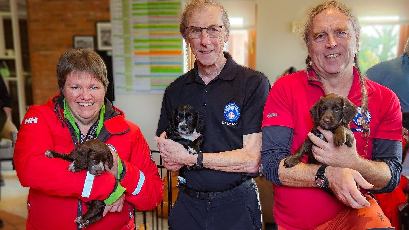 Sarah Garner, Ian Yates, Graeme Poole and puppies, dressed in branded clothing, smiling at the camera, holding a puppy each