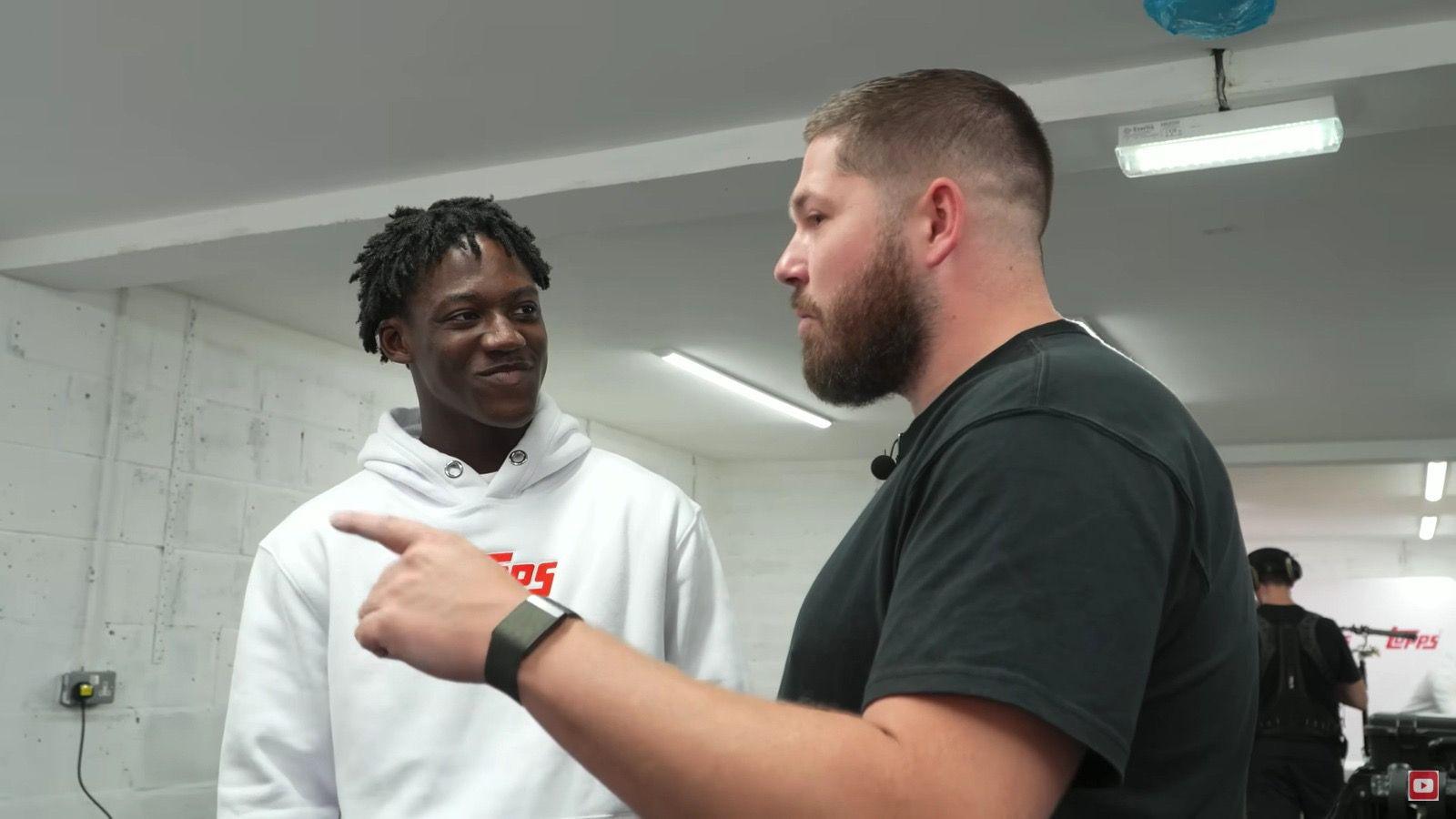 Kobbie Mainoo wearing a white jumper and John Nellis wearing a black top, John is pointing