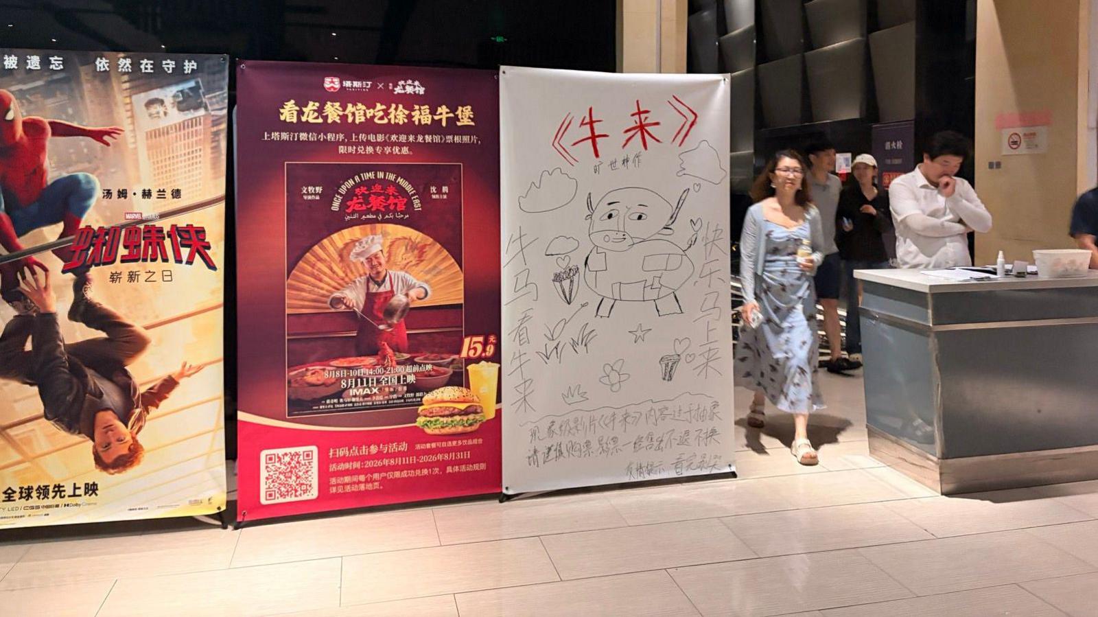A hand drawn poster of Niu Lai sits next to other movie posters including the latest Spiderman movie at a Chinese cinema complex