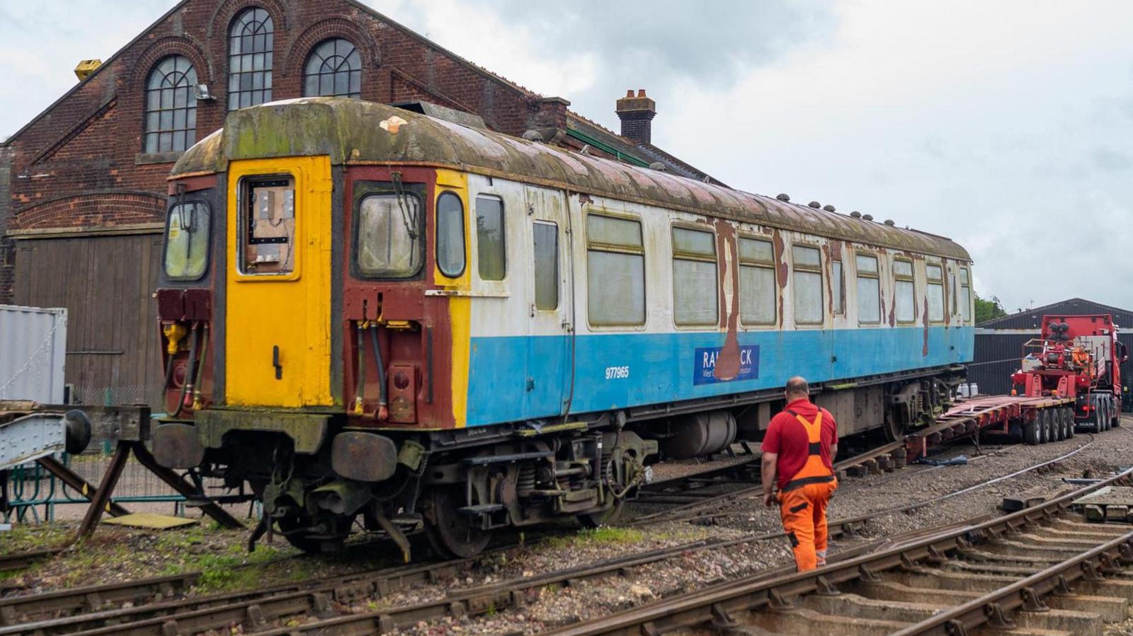 The Clacton Express is pictured after it had first arrived at East Anglian Railway Museum via a lorry. The train is pictured being moved on to the train tracks. A worker in a red top and orange hi-vis overalls watches on.