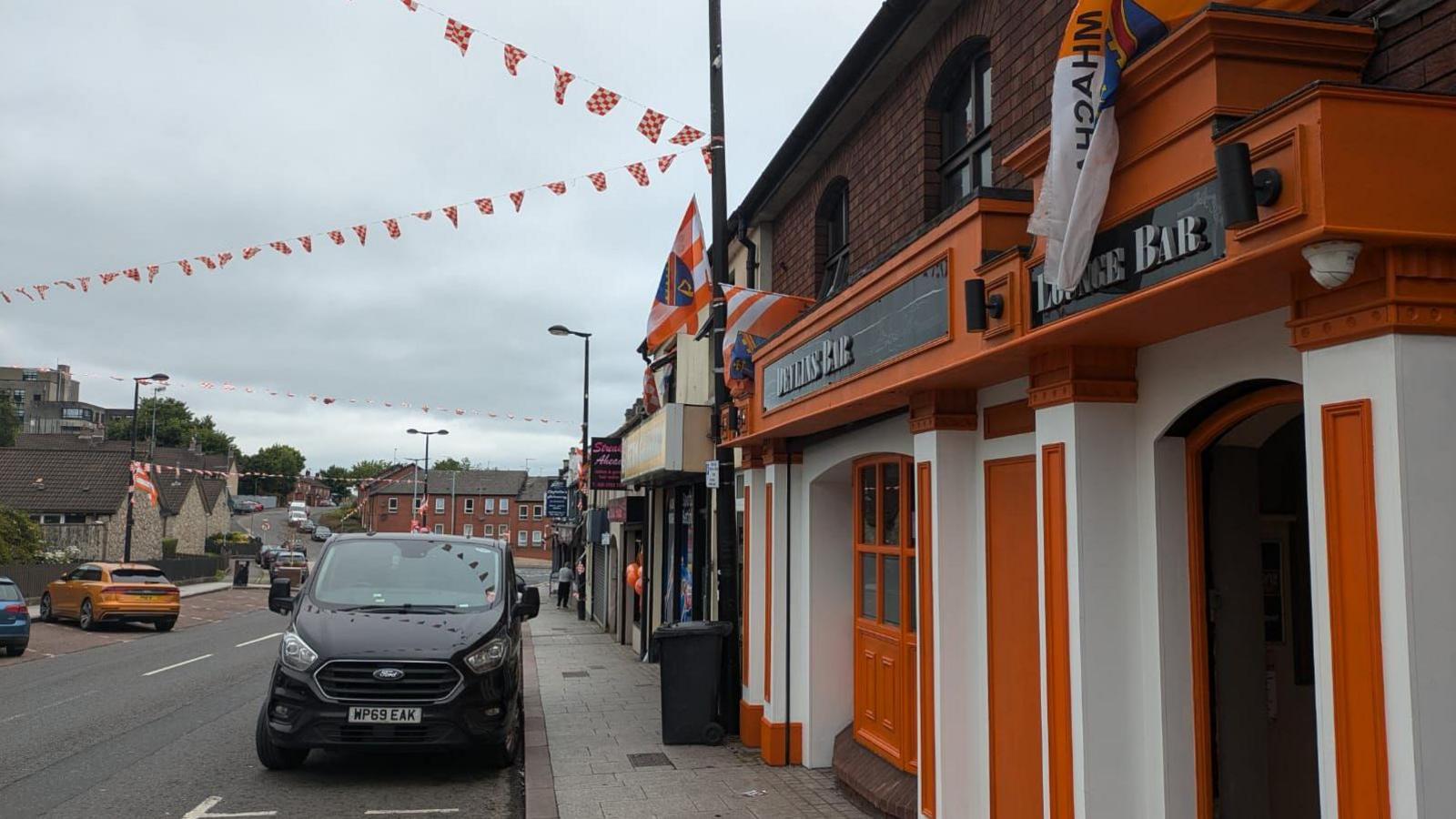 A pub painted orange and white and with orange and white bunding over the road that it is on