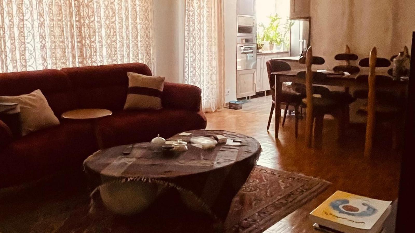Living room with a sofa, coffee table and rug, with the curtains closed, and a dining table and kitchen in the background.