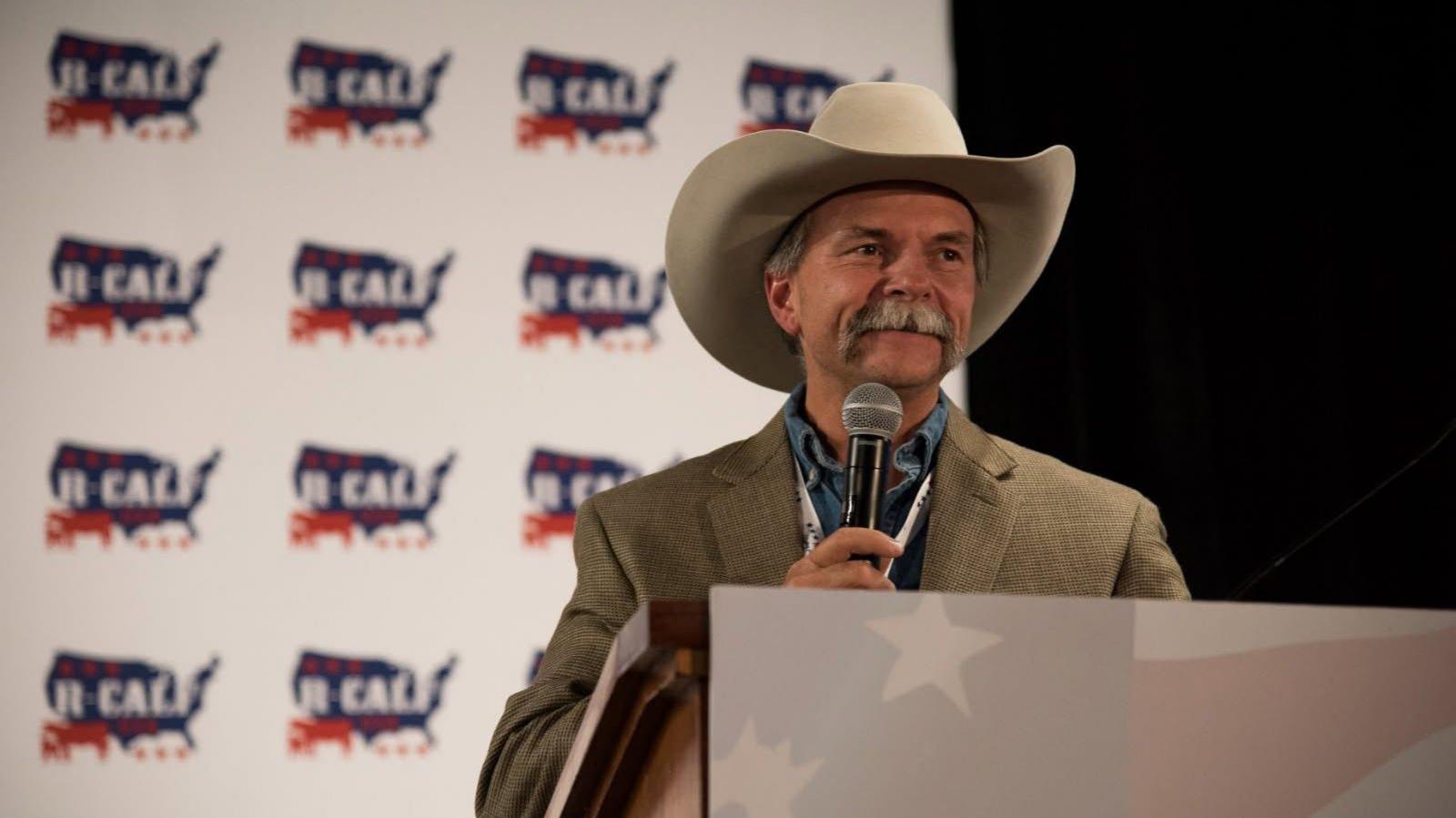 A man wearing a cowboy hat speaks into a microphone.