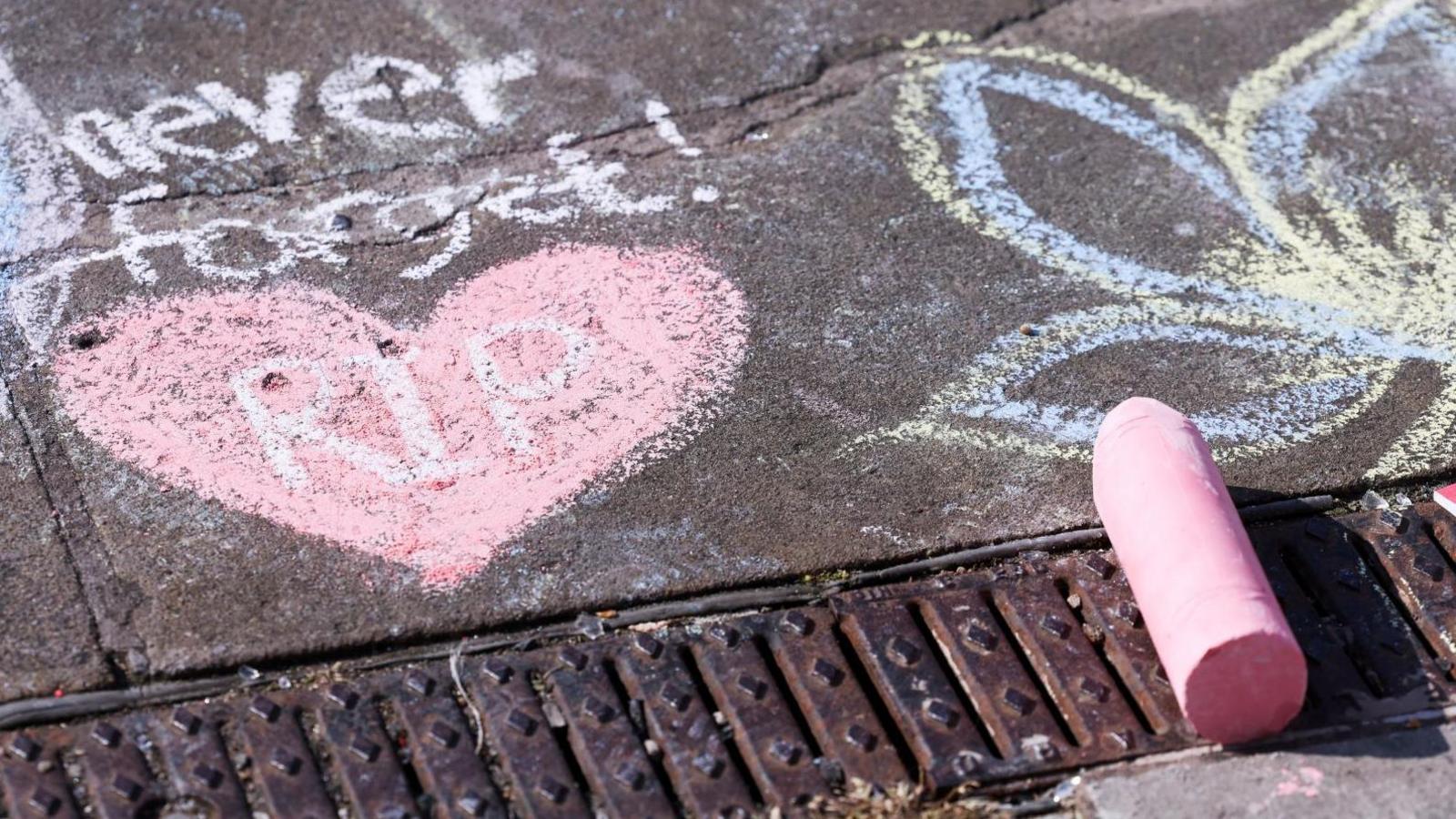 Chalk drawings on the pavement in Southport. One message reads 'never forget', another is a pink heart with the words RIP written in it, a third is a purple and yellow flower