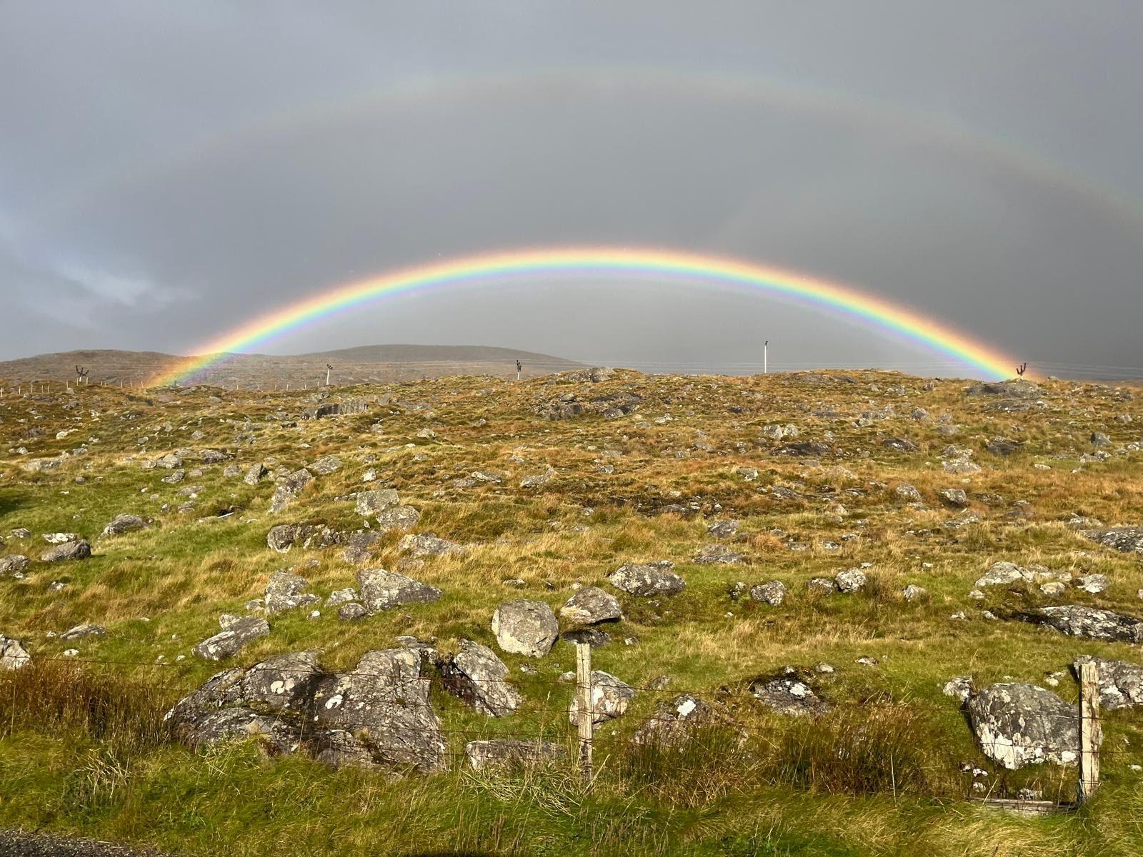 A rainbow shining over grass and hills