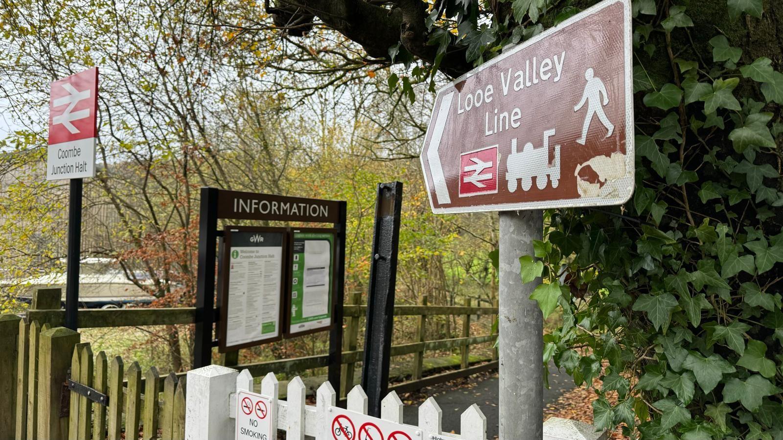 A white wooden gate in front of a rail line, with signs saying Looe Valley Line and another saying Coombe Junction Halt 