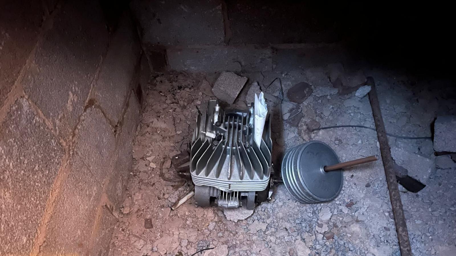 A small motor engine on a rough concrete and gravel floor inside a dimly lit brick enclosure under the floorboards of a house in Devon. 