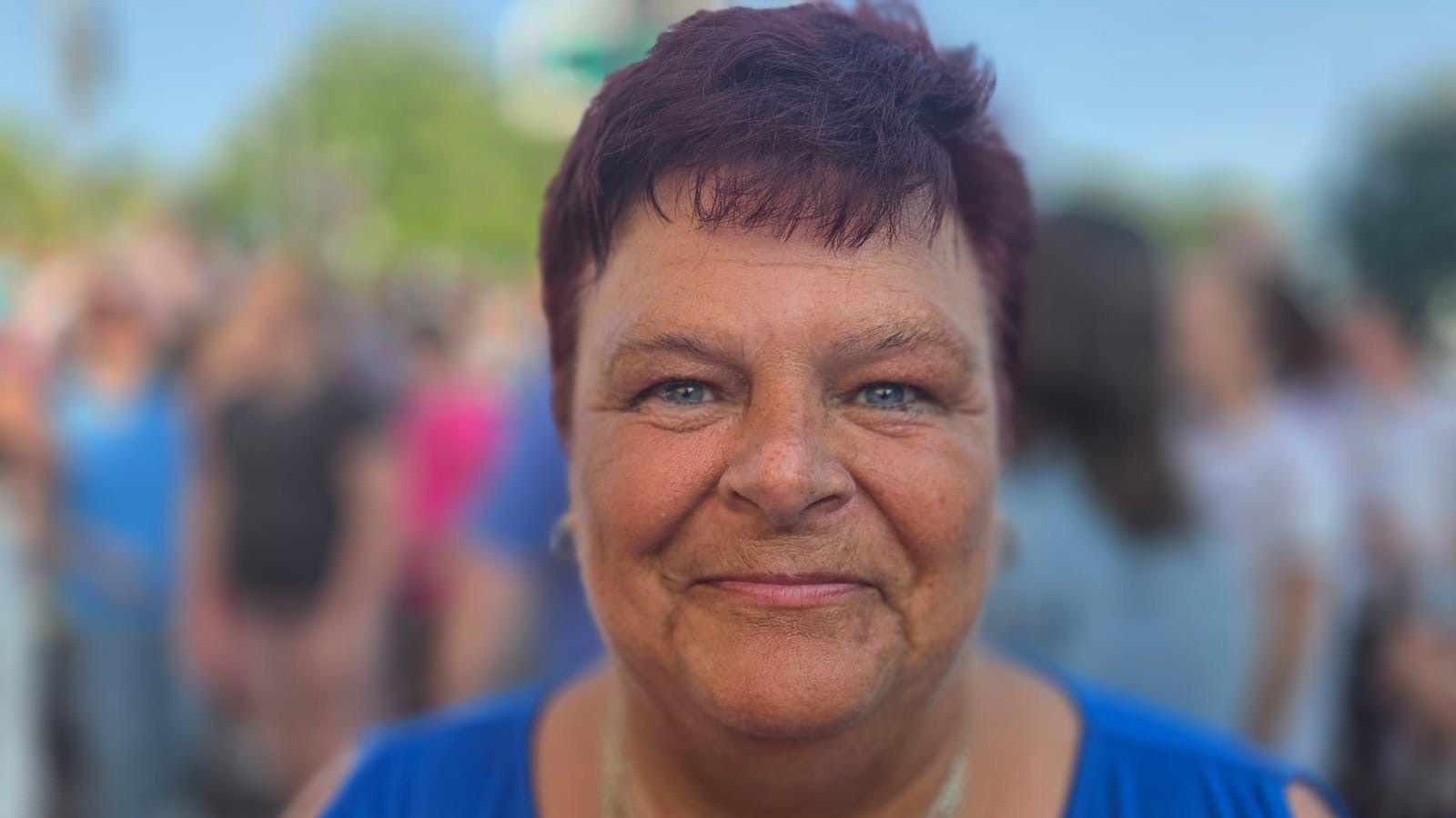 A woman with short dark purple hair smiling at the camera wearing a blue top.