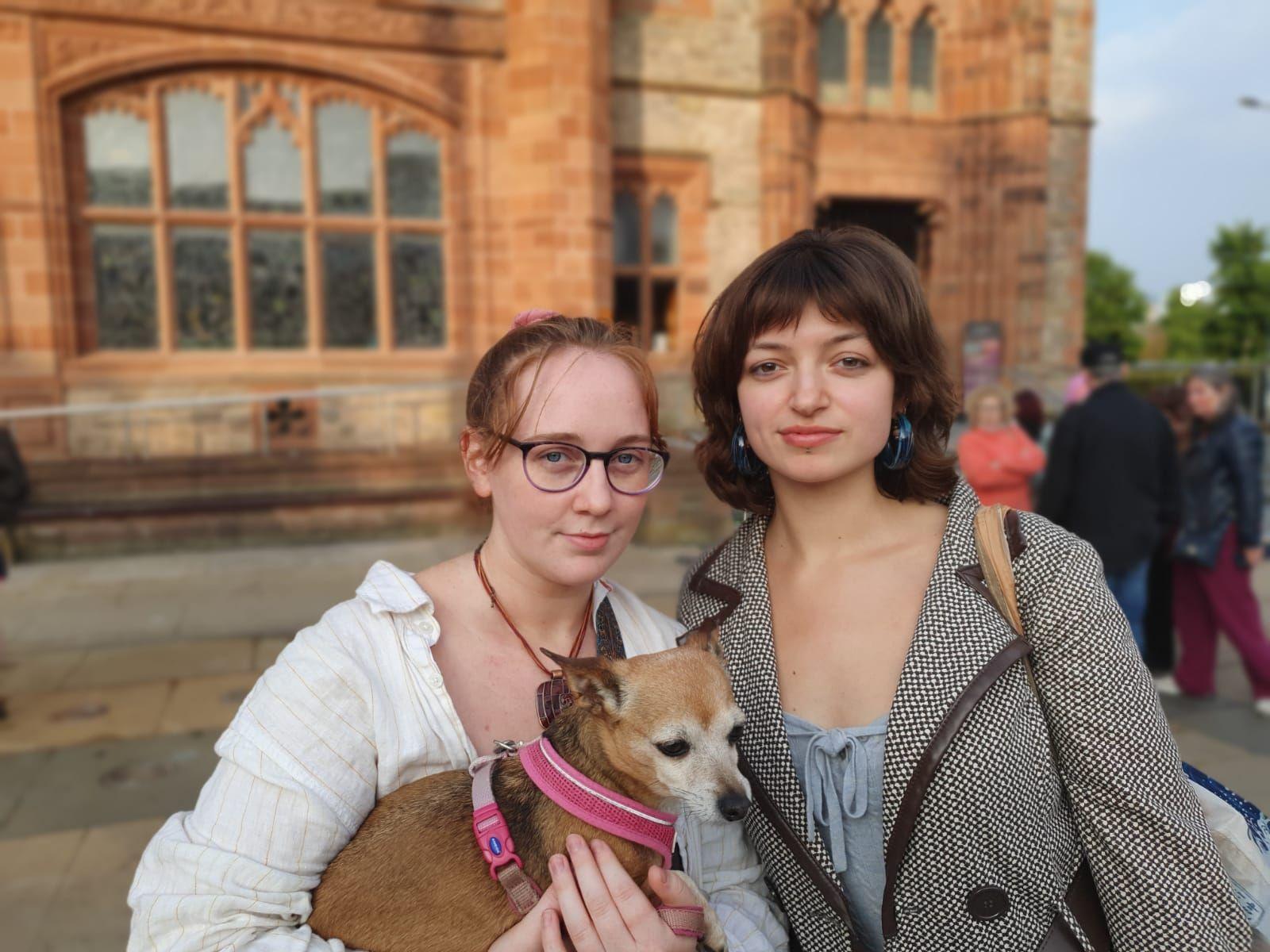 Cara Gilliland and Aoibheann Armstrong stand in front of Derry's Guidhall. Cara is holding a dog