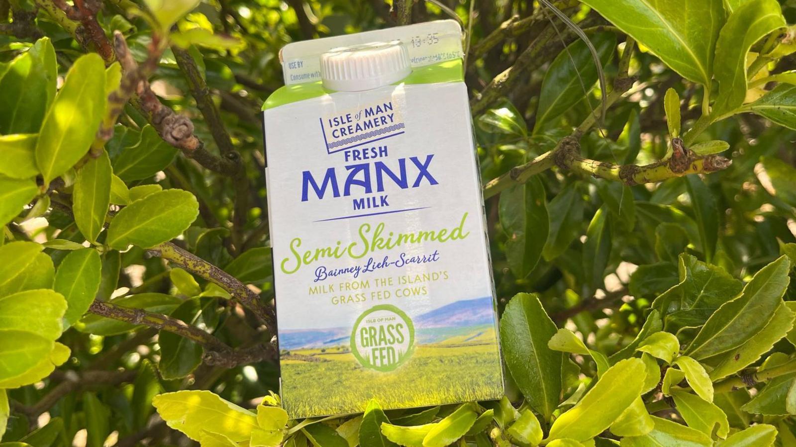 A pint of Manx milk with green labelling rests in front of a green bush.