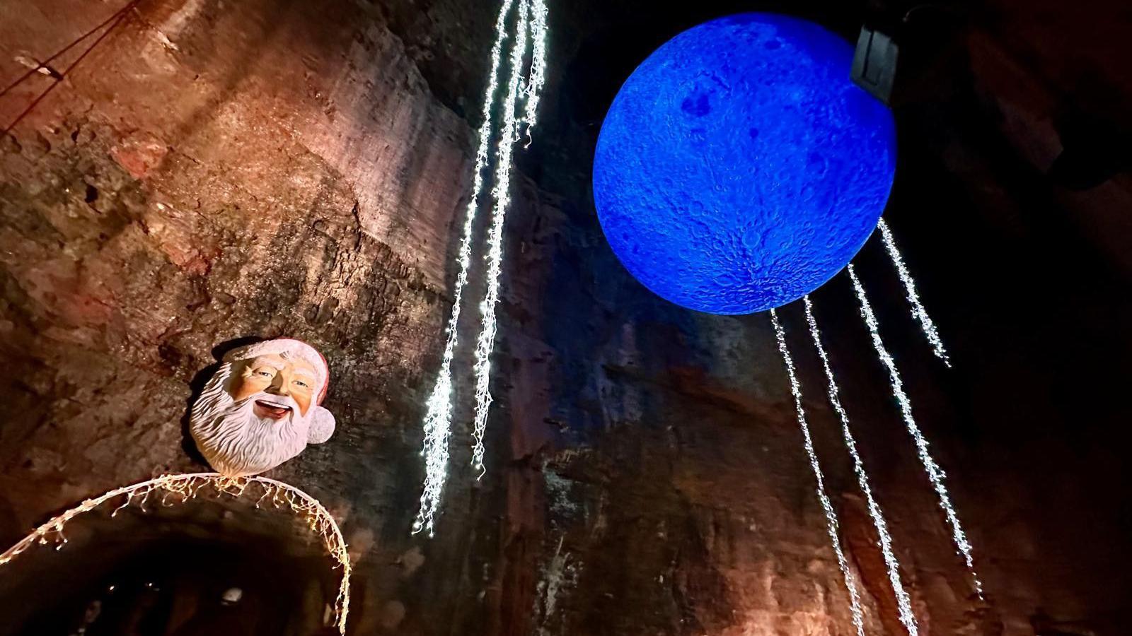 An internal picture of the Christmas attraction at Wookey Hole caves, with a large Santa head on the wall and thousands of fairy lights hanging from the cave ceiling