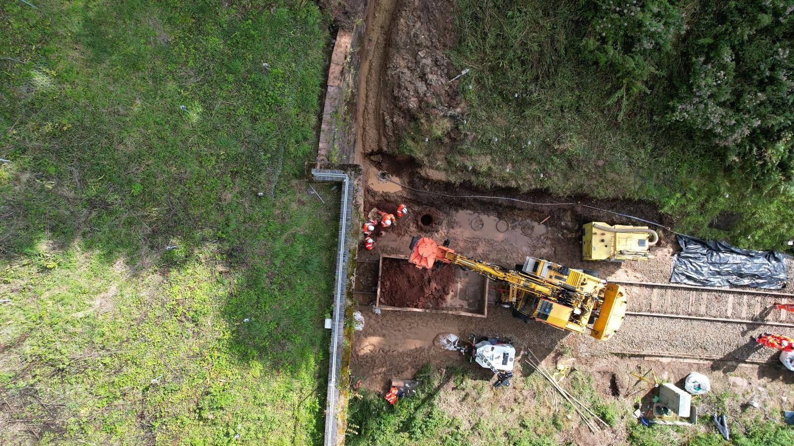 View from above of a small yellow digger depositing wet mud from a traintrack into a skip, which is blocking a tunnel