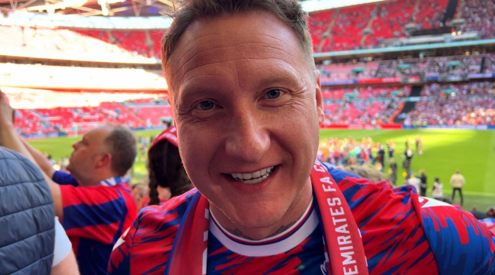 A Crystal Palace fan in a club t-shirt smiles at the camera