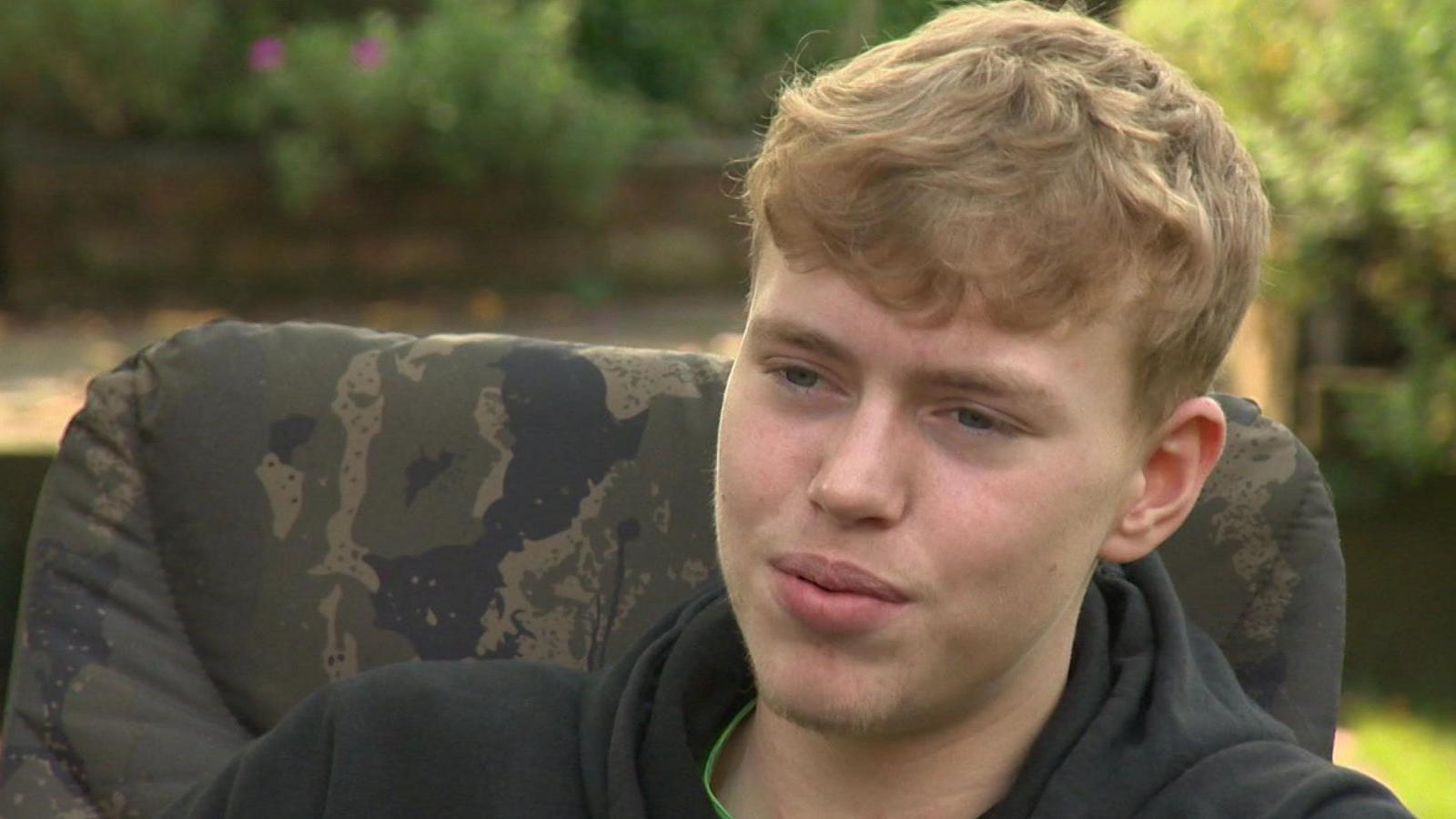 Max Johnson, was dark blonde hair and wearing a black hoodie, sits on a camping chair in a garden and speaks to the camera