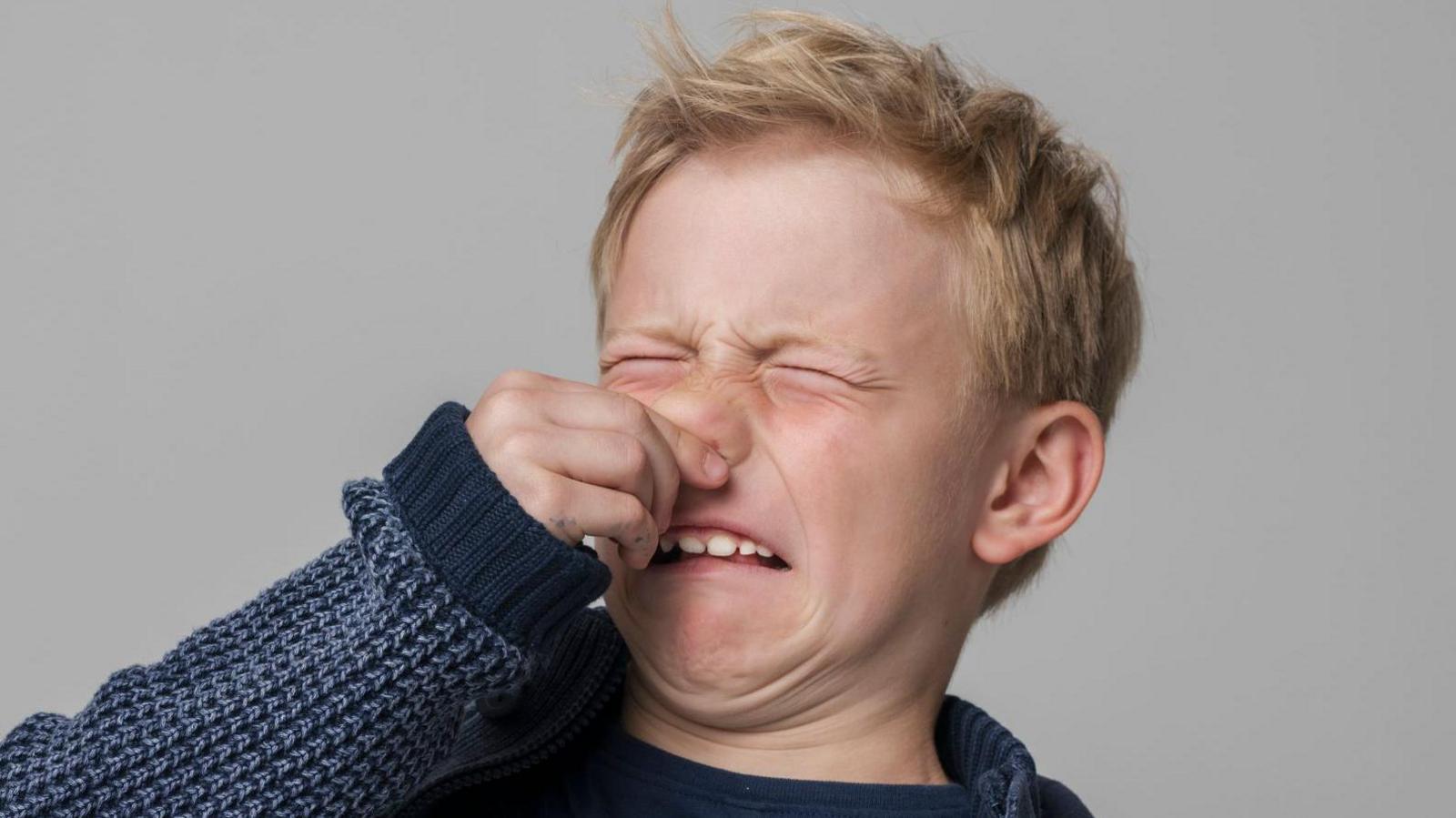 A young boy makes a funny face with his hand over his nose as if he's caught an unpleasant smell. 