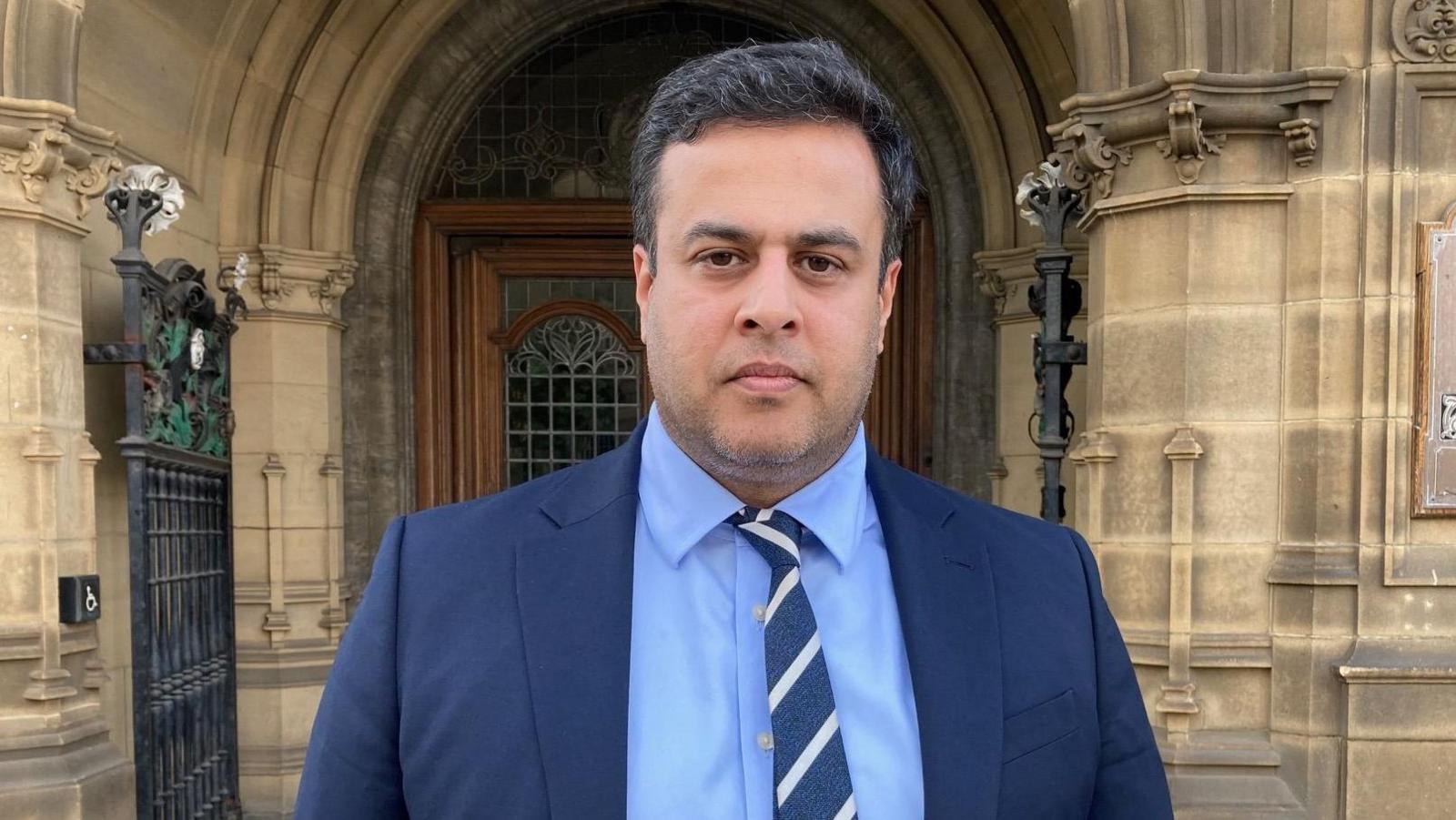 Nadeem Ahmed, leader of the Wakefield Conservative and Independent Group, wears a dark blue jacket with a light blue shirt and white and blue striped tie