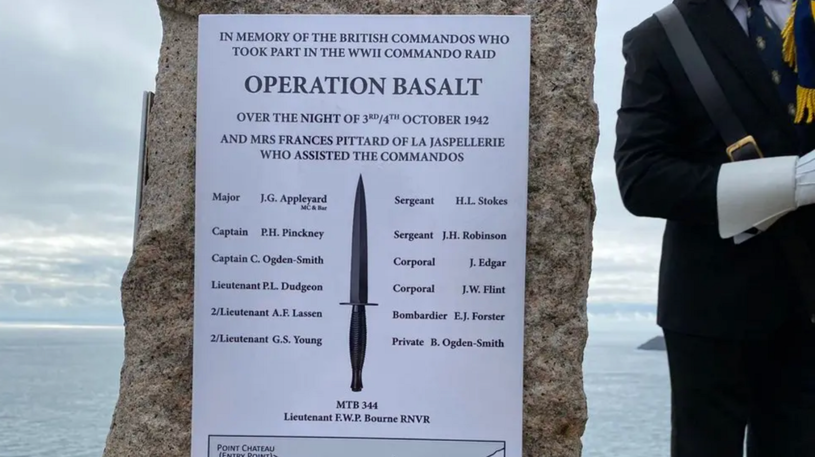 A white memorial plaque that lists the names of the officers involved in Operation Basalt. In the centre, there is a picture of the commando dagger