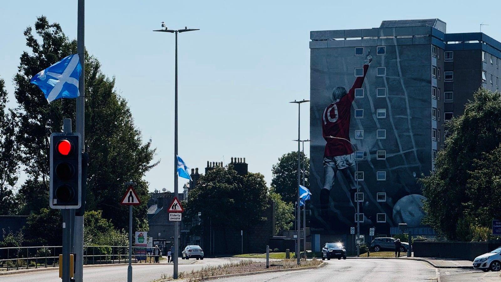 Saltires in Aberdeen streets with a high-rise in the distance featuring a mural of footballer Denis Law.