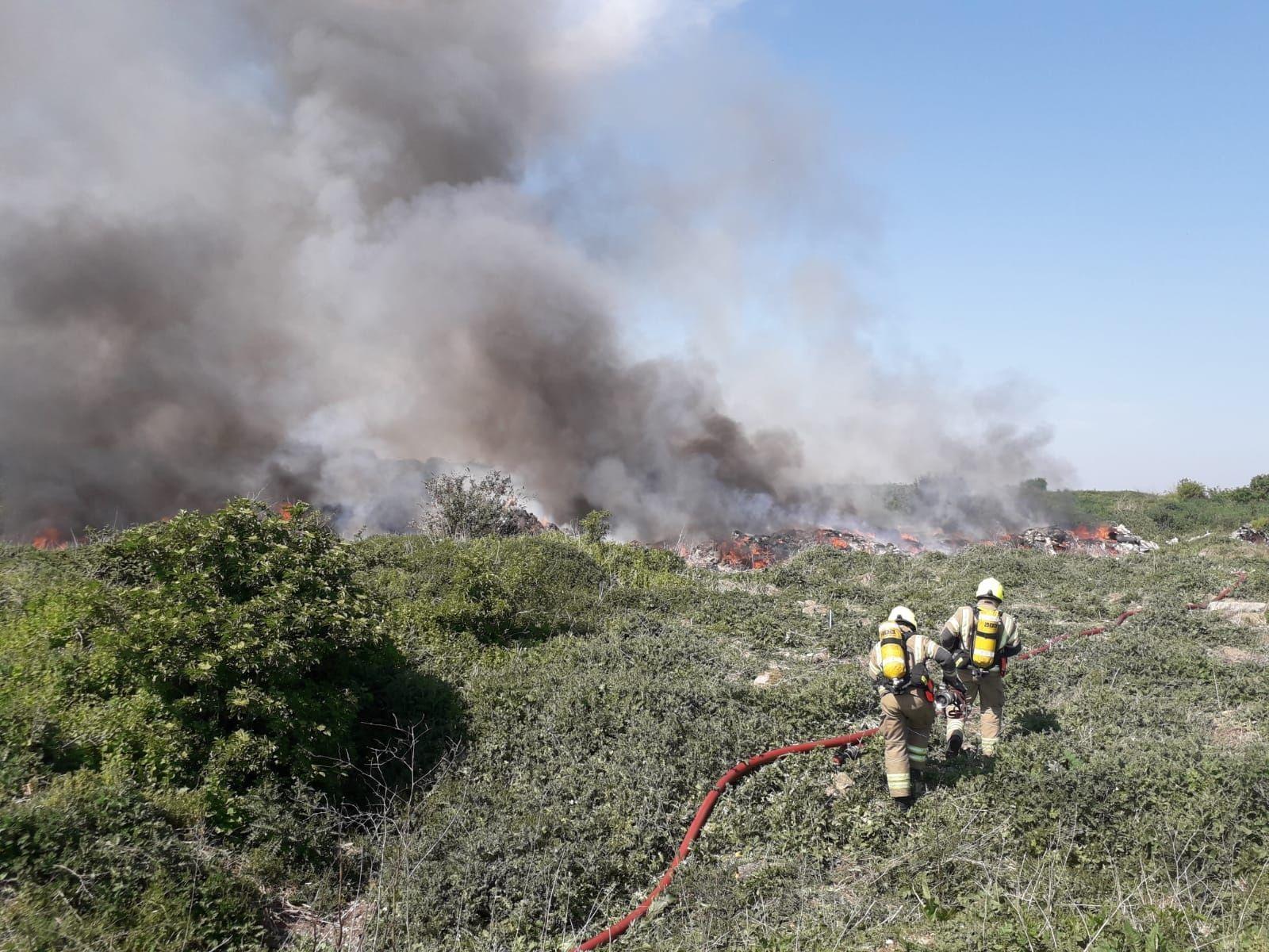 Two firefighters use a hose on a fire on scrubland