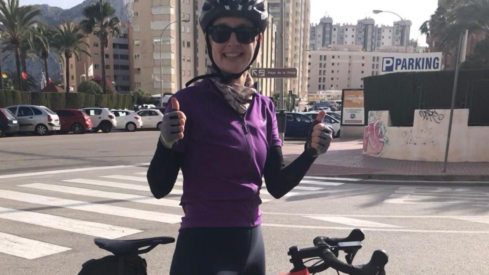 Jillian Egan, who is wearing a purple cycling jersey and a black helmet. She is stood next to her bike on the roadside.